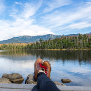 Lakeside mountain view over someone's outstretched legs, wearing hiking boots